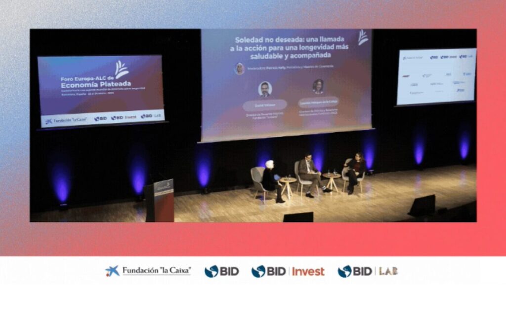 Conferencia por las personas mayores. Tres personas sentadas en un escenario con una presentación de fondo.